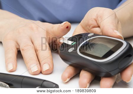 Closeup female hands using glucometer scanner on finger with blood sample