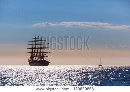 The world's largest sailing ship with five masts leaves at sunset in the open sea.