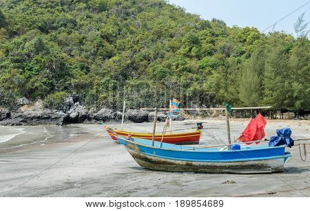 Small woodenl fishing boats (Longtail boats) anchored on beach at low tide in Thailand
