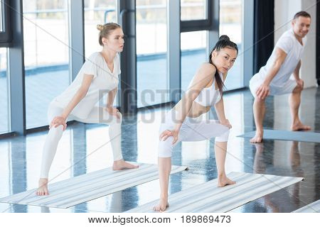girls in white clothes doing sumo pose (rudrasana) with instructor indoors