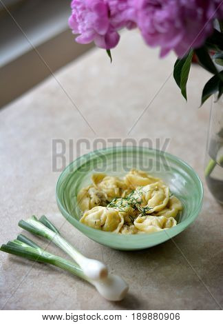Dumplings in the green bowl on the stone table with greens in details