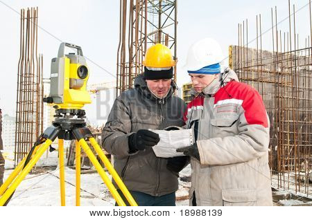 Discussing Surveyor worker and assistant at construction site in winter with theodolite equipment