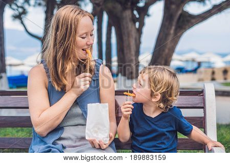 Mom And Son Eat Fried Sweet Potatoes In The Park. Junk Food Concept