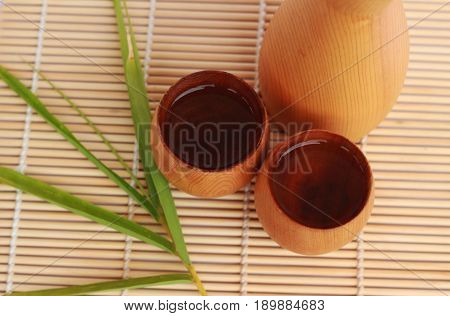 SAKE liqueur in a brown wooden bottle on a light brown background.