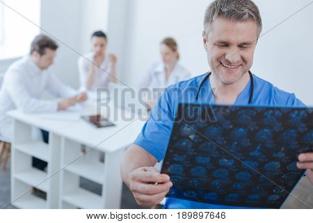 Examining positive mrt result . Confident attentive optimistic neurologist working at the hospital and examining mrt scan results while colleagues sharing opinions in the background