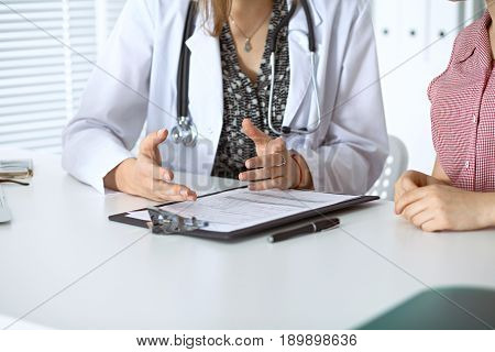 Doctor and patient sitting at the desk. Physician pointing into medical history records and explaining something to young woman. Medicine and health care concept.