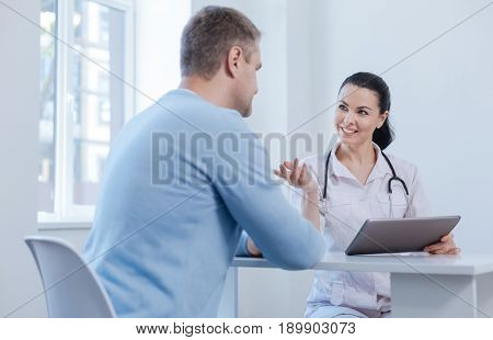 Guiding you in new innovative treatment. Delighted involved skillful doctor enjoying appointment in the hospital and using digital gadget while expressing happiness