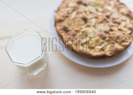Fresh baked apple pie on a white plate and a glass of milk on a light wooden background