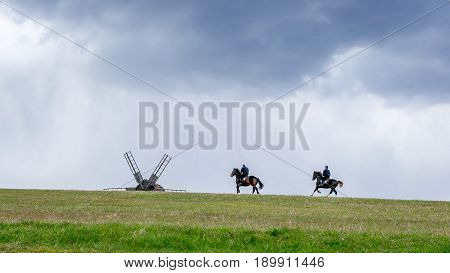 Ancient traditional wooden windmill beautiful spring rural landscape with horsemen on the horizon. National Museum Pirogovo in the outdoors near Kiev.
