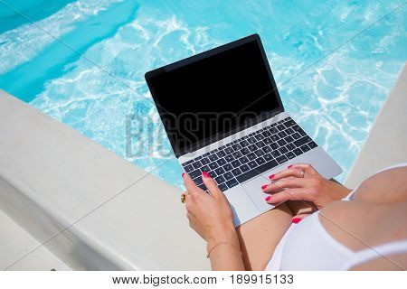 Girl wearing bikini working with laptop by the pool