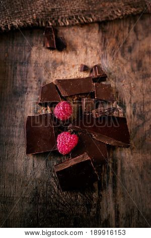 Broken chocolate bar with red ripe raspberries on dark brown background close up macro