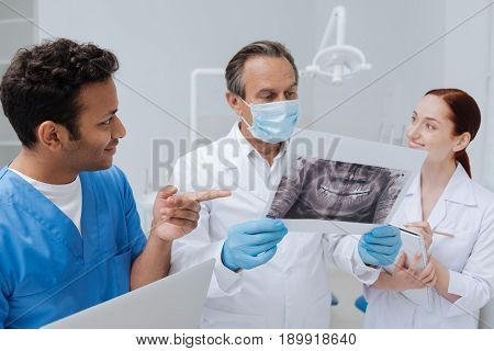 Great results. Smiling intern standing in semi position holding laptop in right hand while raising his forefinger