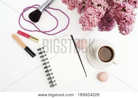 Spring lilac flowers on workdesk female home office with note and coffee white background top view