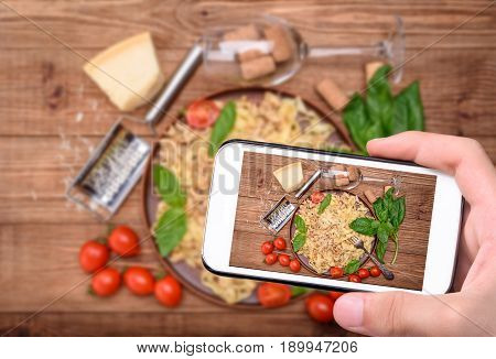 Hands taking photo traditional Italian pasta, served with a meat-based sauce with smartphone.