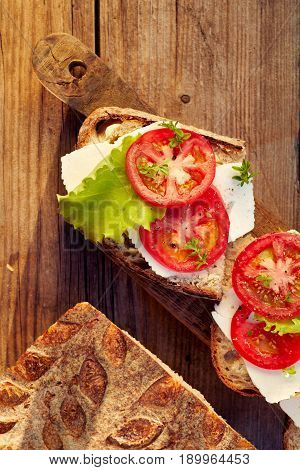 Sandwiches with cheese, tomato and lettuce on a rustic wooden table, top view