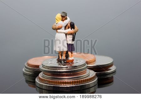 miniature businessman people and family hugs together standing on the coins