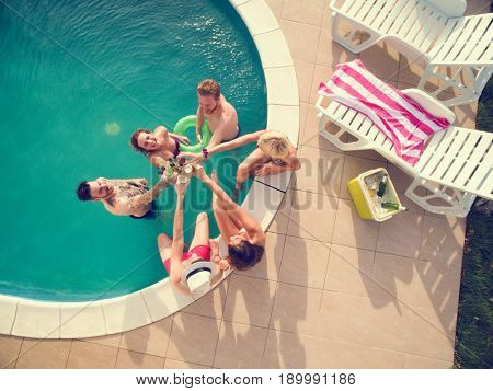 Top view of young cheerful girls and boys in swimming pool toasting with cold bear 