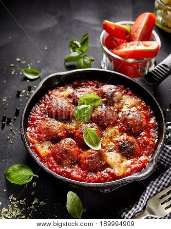 Meatballs in tomato sauce with addition cheese and fresh basil on iron pan, black background