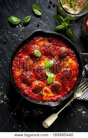 Meatballs in tomato sauce with addition cheese and fresh basil on iron pan, black background, top view