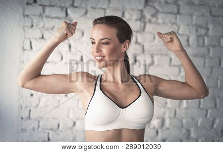 Young Strong Fit Woman Showing Bicepses Portrait In Gym, Looking Away