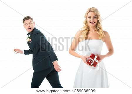 Happy Beautiful Bride Holding Gift Box, While Tricky Groom Imitating Running Away Isolated On White