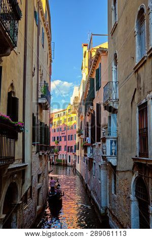 VENICE, ITALY - JUNE 27, 2018:  Narrow canal between colorful old houses with gondola boat with tourists and gonolier in Venice, Italy