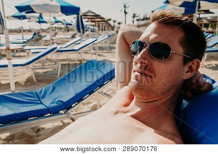 Young Attractive Well-groomed Man With Tanned Skin Sitting On The Beach