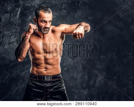 Professional Fighter Showing Kick Fighting Technique. Studio Photo Against A Dark Textured Wall