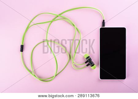 Green Headphones Connected To A Smartphone Isolated On A Pink Background. Accessories For Individual