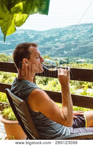 A Handsome Adult Man Sits On A Farm And Tastes A Glass Of White Wine. Sunny Day, Cyprus.