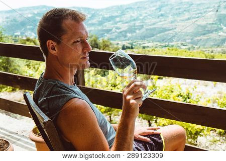 A Handsome Adult Man Sits On A Farm And Tastes A Glass Of White Wine. Sunny Day, Cyprus.