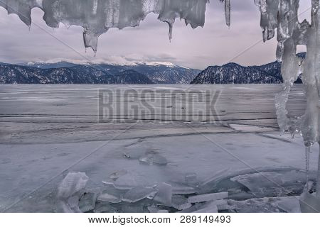 Winter Landscape With A Frozen Lake In The Mountains, Ice And A Curtain Of Icicles Against The Cloud