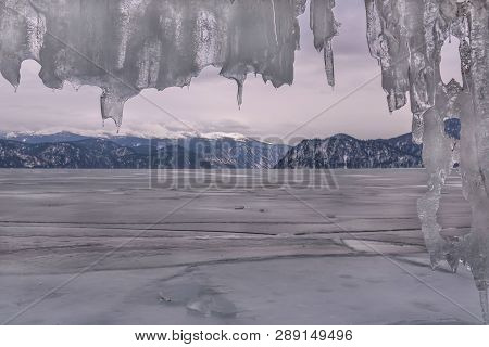 Winter Landscape With A Frozen Lake In The Mountains, Ice And A Curtain Of Icicles Against The Cloud