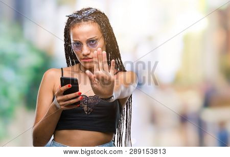 Young braided hair african american with birth mark using smartphone over isolated background with open hand doing stop sign with serious and confident expression, defense gesture
