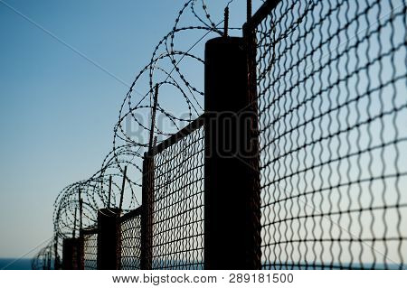 Razor Barbed Wire On High Steel Fence On Blue Sky And Sea Background