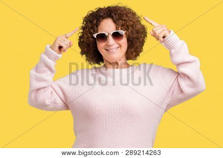 Beautiful middle ager senior woman wearing pink sweater and sunglasses over isolated background Smiling pointing to head with both hands finger, great idea or thought, good memory