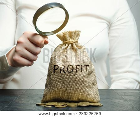 Businesswoman Holds A Magnifying Glass Over A Money Bag With The Word Profit. Analysis Of The Budget