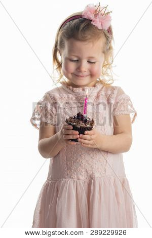Little Girl In Pastel Pink Dress And Crown Headband Holding Chocolate Cupkake With Candle In It, On 