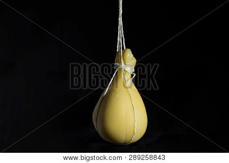 Typical Italian Cheese Caciocavallo Ripens In Ropes In A Hanging State On A Dark Background.