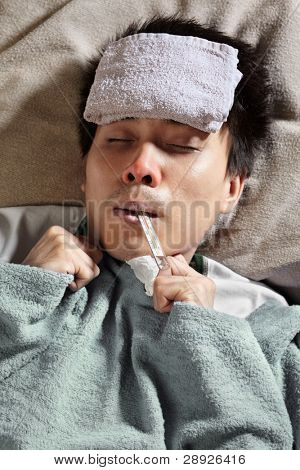 Um doente dormindo masculino com molhar a toalha na testa para reduzir a febre alta alta