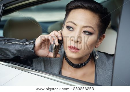 Face Of Beautiful Serious Woman Looking Though Car Window And Talking On Phone