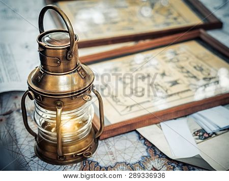Old Brassy Ship Lantern Stands On A Map Of The Seas Near Pictures With The Image Of Sea Knots