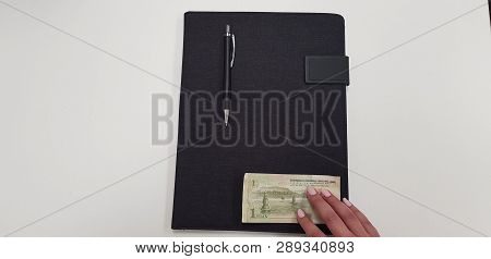 Woman Holds Fingers On One Yinhang Banknote On Black Folder With Pen On It