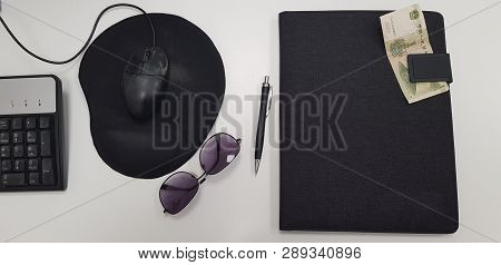 Office Tools On White Table Near Pen Sunglasses And Black Folder With One Chinese Banknote