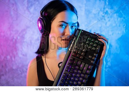 Young Sexy Disco Girl Wearing Gaming Headset Holding Gaming Keyboard. Room Lit In Retro, Retrowave O