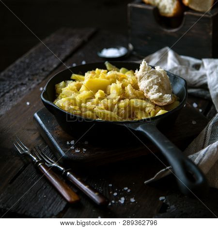 Homemade Roast Potatoes In Cast-iron Pan Standing On Wooden Board On Rustic Dark Wooden Table With P