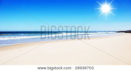 Ren åben stranden med solen i en smuk blå himmel