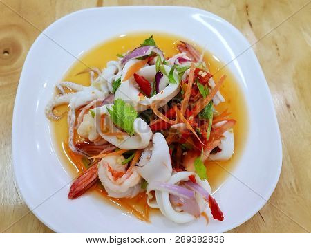 Thai Food Style, Top View Of Spicy Thai Seafood Salad On White Plate On Wooden Table In Restaurant, 