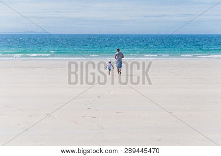Father And Son Running Towards The Atlantic Ocean On The Beach In Finistere France