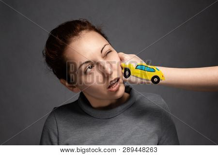 A Young Girl Is Hit In The Face With A Fist That Represents A Car .the Concept Of Accidents And Insu